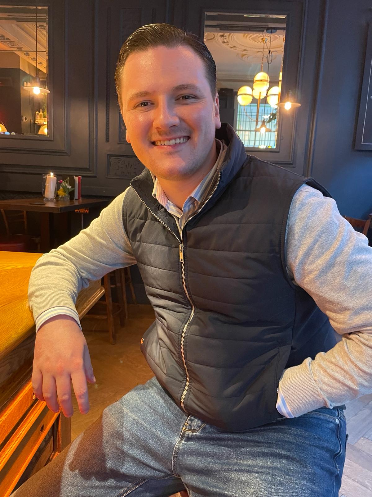 A young man sitting in a bar/restaurant smiling